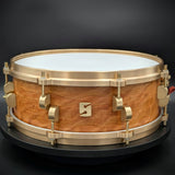 A 5" x 14" North American Quilted Cherry snare drum with brass hardware and a white drum head, displayed on a black background.